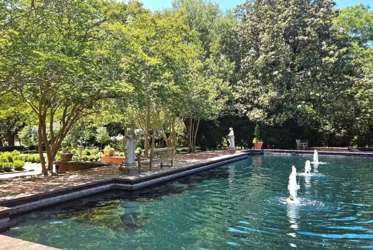 Formal garden reflecting pool with water fountains, classical statues, benches, and mature shade trees, sunny day, no people, Aiken, SC