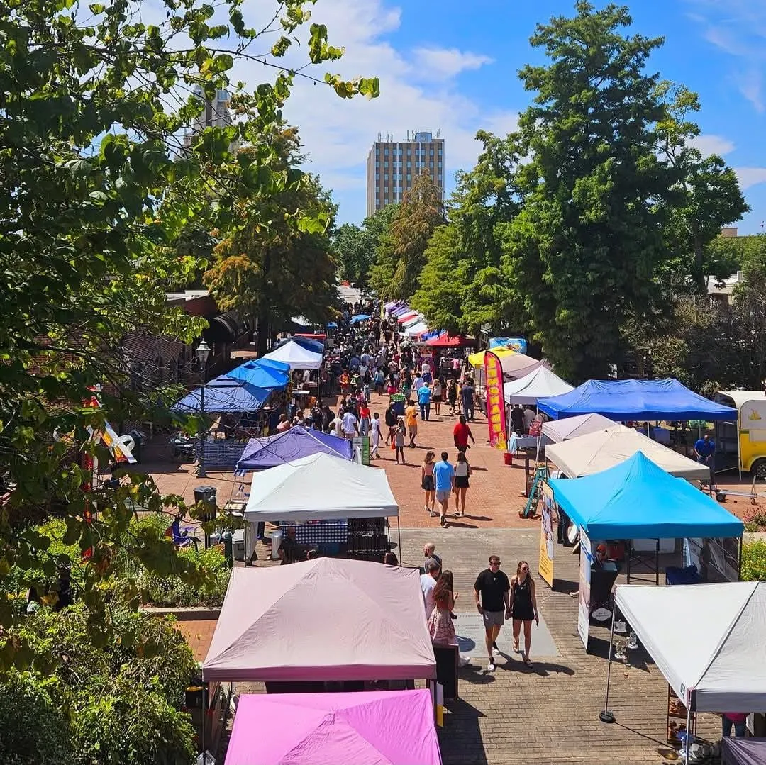 Elevated wide view of a downtown pedestrian street market with rows of colorful vendor tents and a crowd of people walking, city high-rise, Augusta, GA