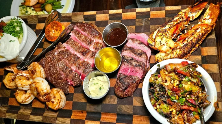 Brinkley's Chop House, Augusta, GA: steakhouse surf and turf platter on wooden board: sliced steak, grilled shrimp, split lobster tail, roasted vegetables, dipping sauces and mashed potatoes
