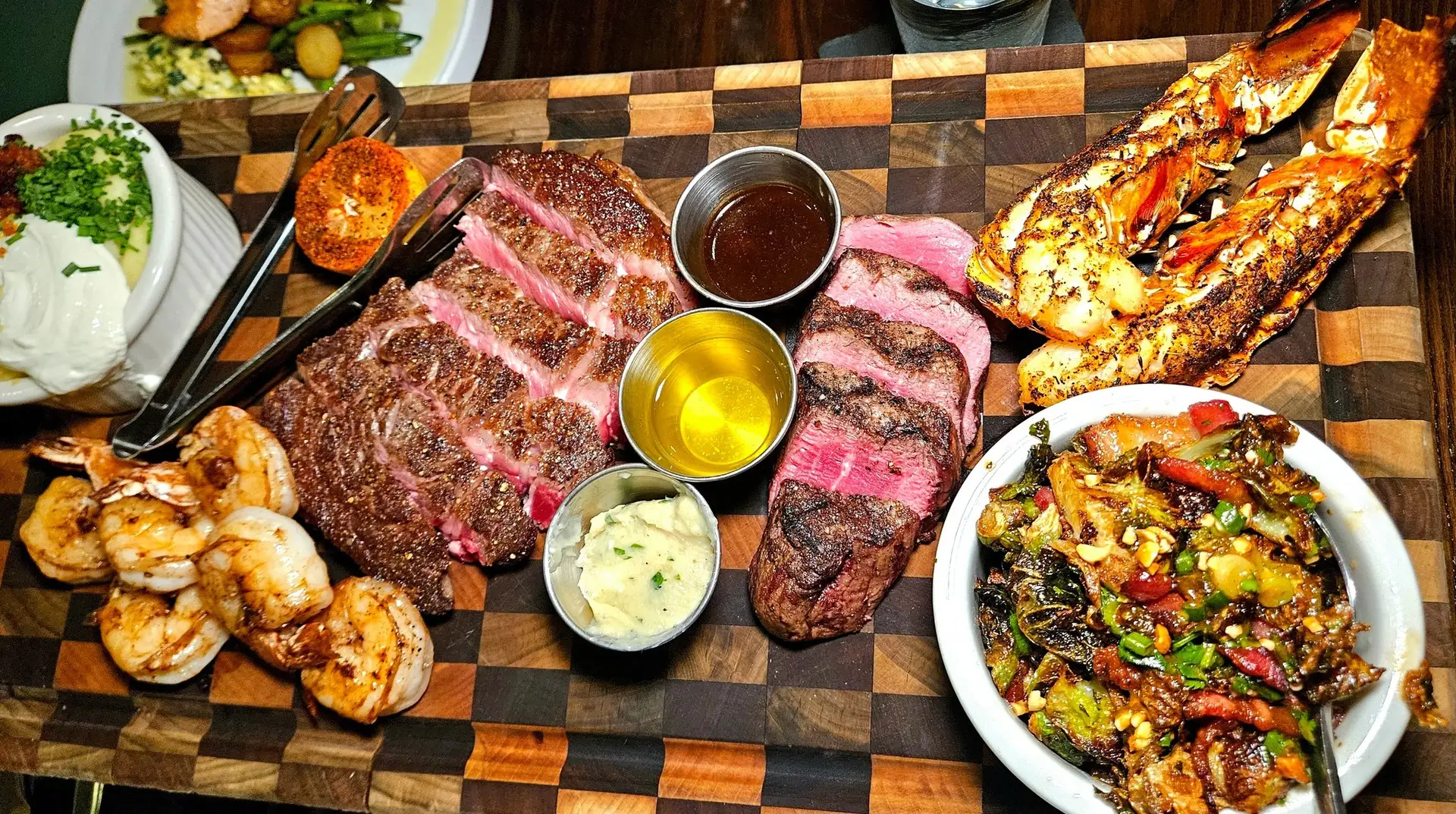 Brinkley's Chop House, Augusta, GA: steakhouse surf and turf platter on wooden board: sliced steak, grilled shrimp, split lobster tail, roasted vegetables, dipping sauces and mashed potatoes
