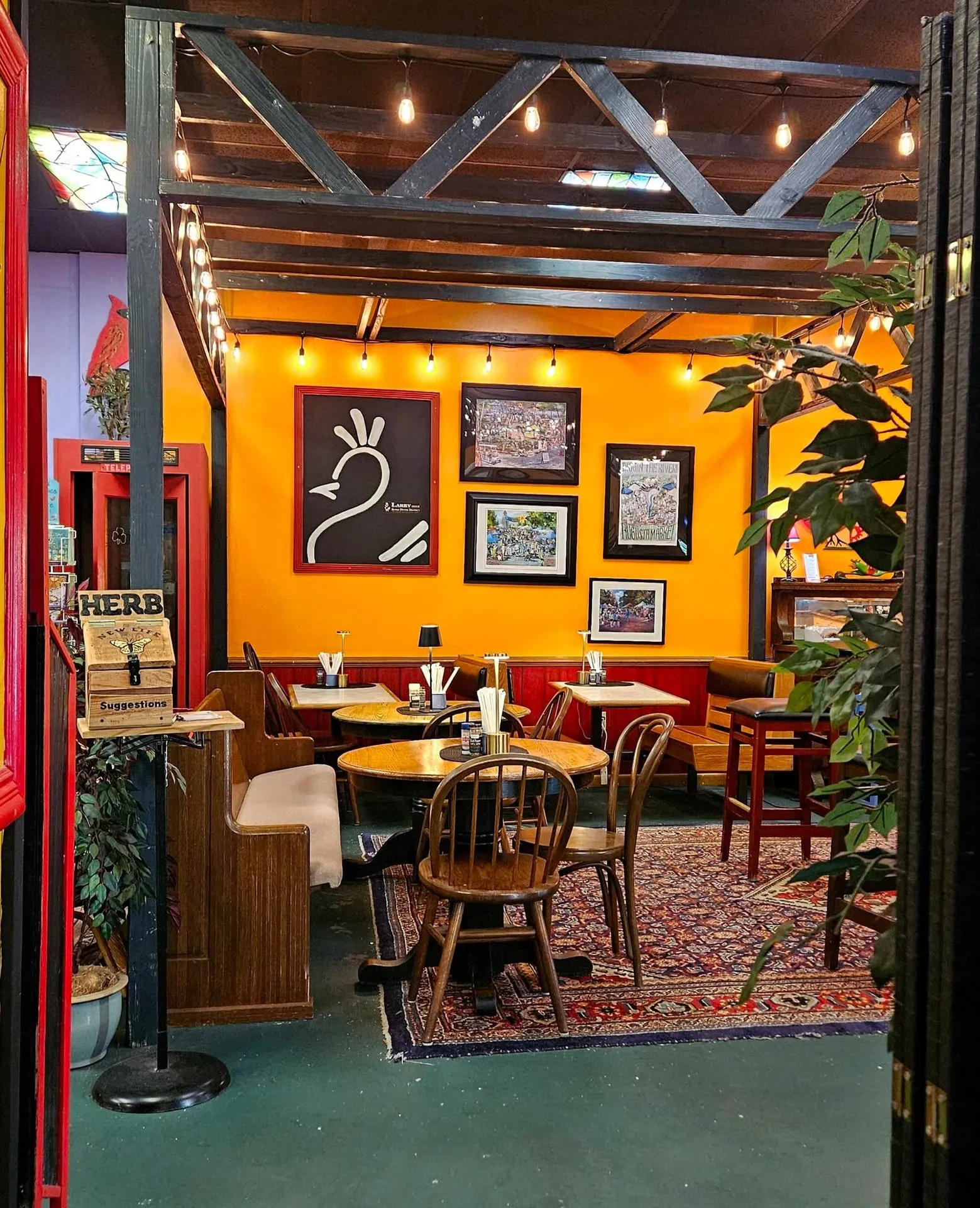 DiChickO's Peri Peri Cafe, North Augusta, SC: restaurant interior with bright orange accent wall, framed artwork including a chicken/rooster silhouette graphic, wooden booth seating, string lights on exposed beam structu