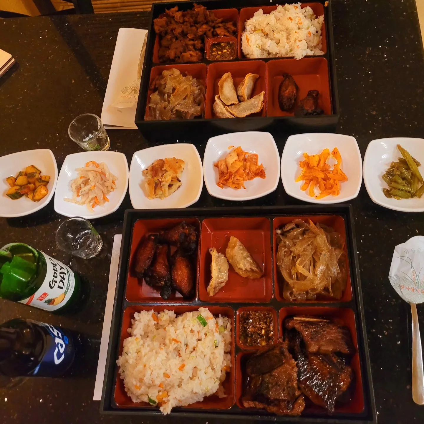 Emashiya Korean Bar-B-Que, Martinez, GA: korean bento box meal spread: fried rice, bulgogi, dumplings, chicken wings, glass noodles, and a row of small banchan dishes including kimchi varieties, with soju/beer bottles