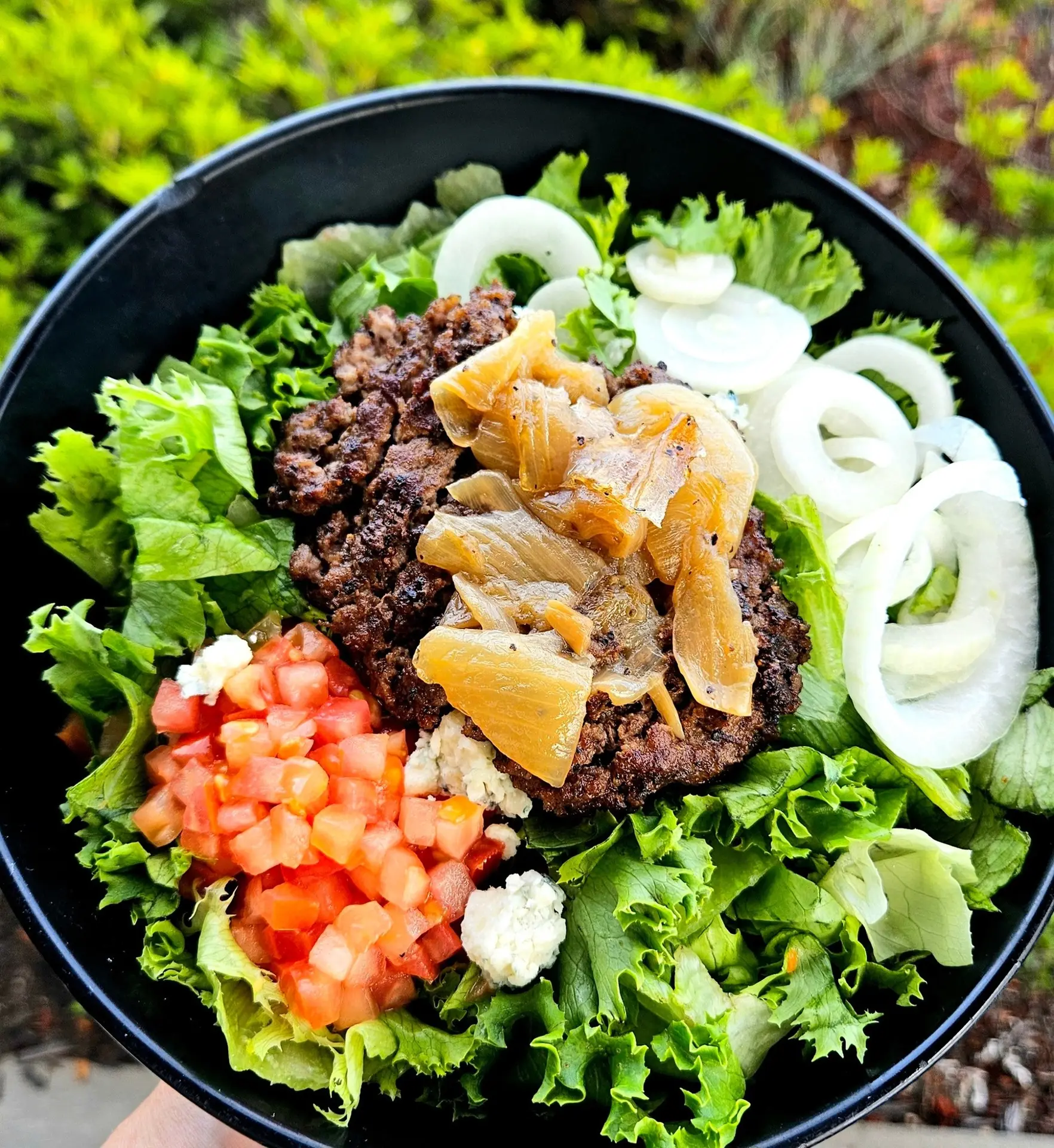 Farmhaus Burger, Aiken, SC: overhead shot of a black bowl containing a grilled burger patty (no bun) over lettuce, with diced tomato, blue cheese crumbles, caramelized onions, and onion rings