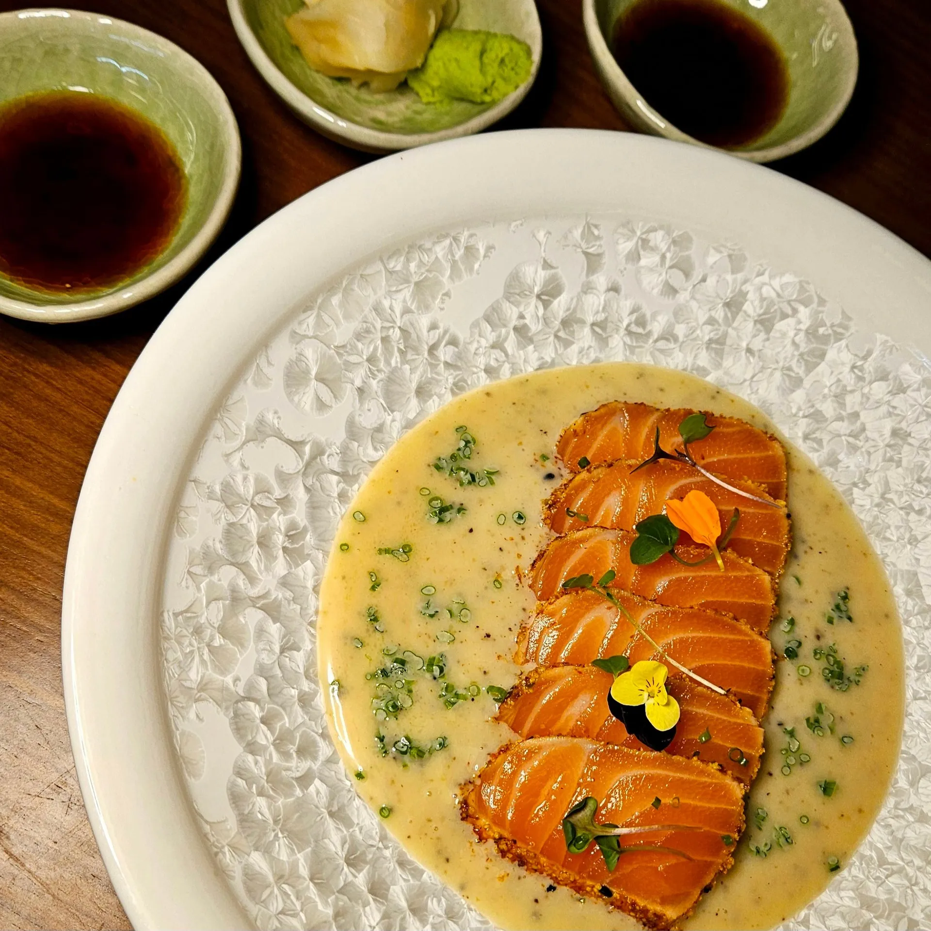 Fukuro Bar Sushi, Evans, GA: overhead shot of sliced salmon sashimi/crudo plated over a creamy citrus sauce with herb garnish, small side dishes of soy sauce, pickled ginger, and wasabi