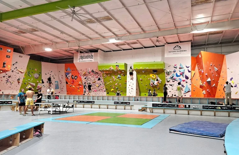 Interior of an indoor rock climbing gym with colorful bouldering walls, crash pads on the floor, and several people climbing and spectating, Grovetown, GA