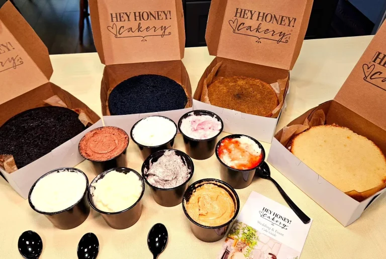 Hey Honey Cakery, Augusta, GA: cake tasting flight boxes branded Hey Honey Cakery, showing four different cake flavors in open kraft boxes and eight small cups of assorted frostings with tasting spoons