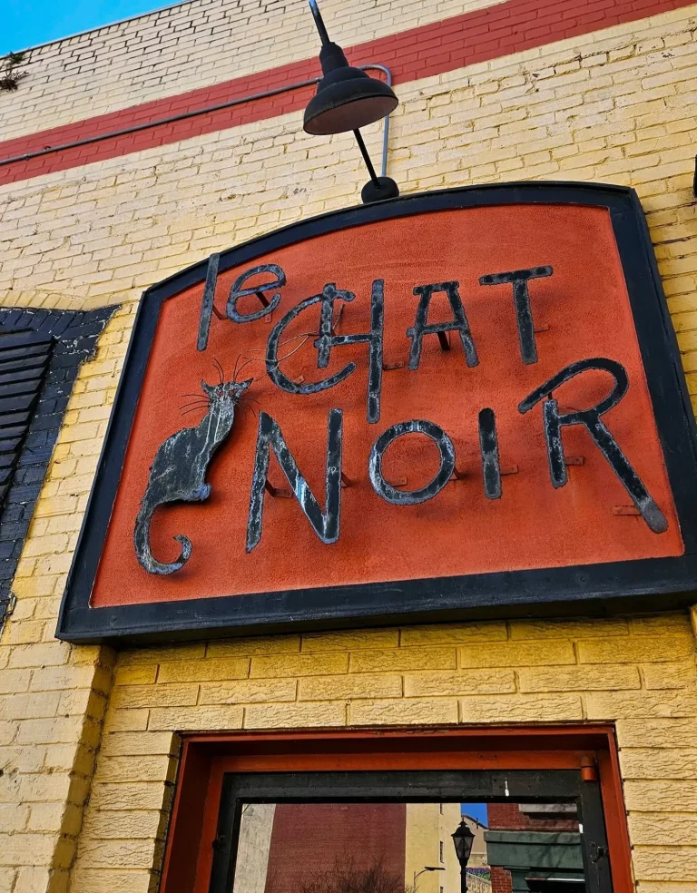 Le Chat Noir, Augusta, GA: storefront exterior sign reading Le Chat Noir with a black cat silhouette icon, mounted on yellow brick building above the entrance