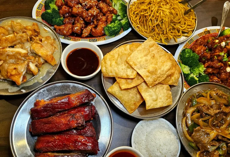 New Ming Wah, Augusta, GA: overhead spread of Chinese takeout dishes: crispy wontons, orange chicken with broccoli, chow mein noodles, beef with onions, white rice, steamed dumplings, sweet-and-sour sauce, and glazed red