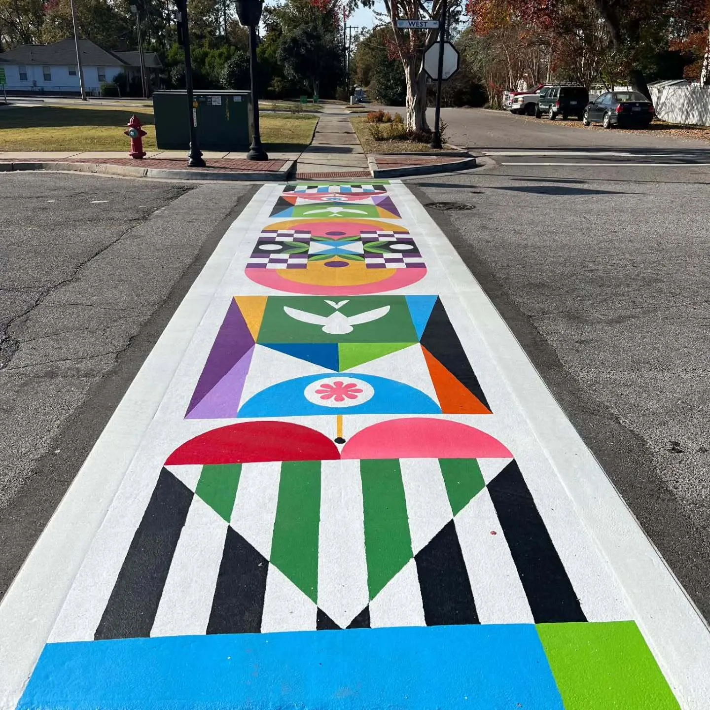 Colorful geometric street mural painted on a crosswalk/street lane, includes a white dove and a heart design, residential street with, North Augusta, SC