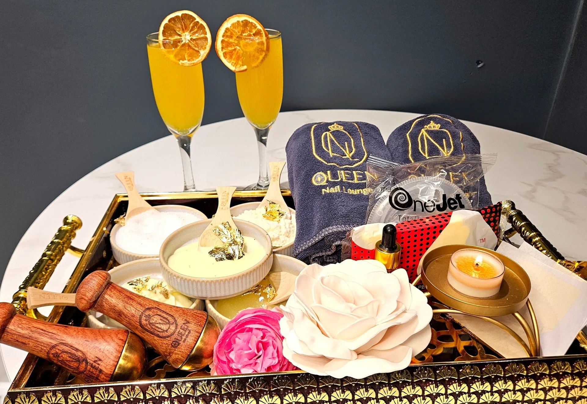 Queen Nails & Lounge, Martinez, GA: nail salon spa tray service: two mimosa champagne flutes garnished with dried orange slices, small bowls of manicure/pedicure lotions, branded Queen Nail Lounge towels, candle, and a d