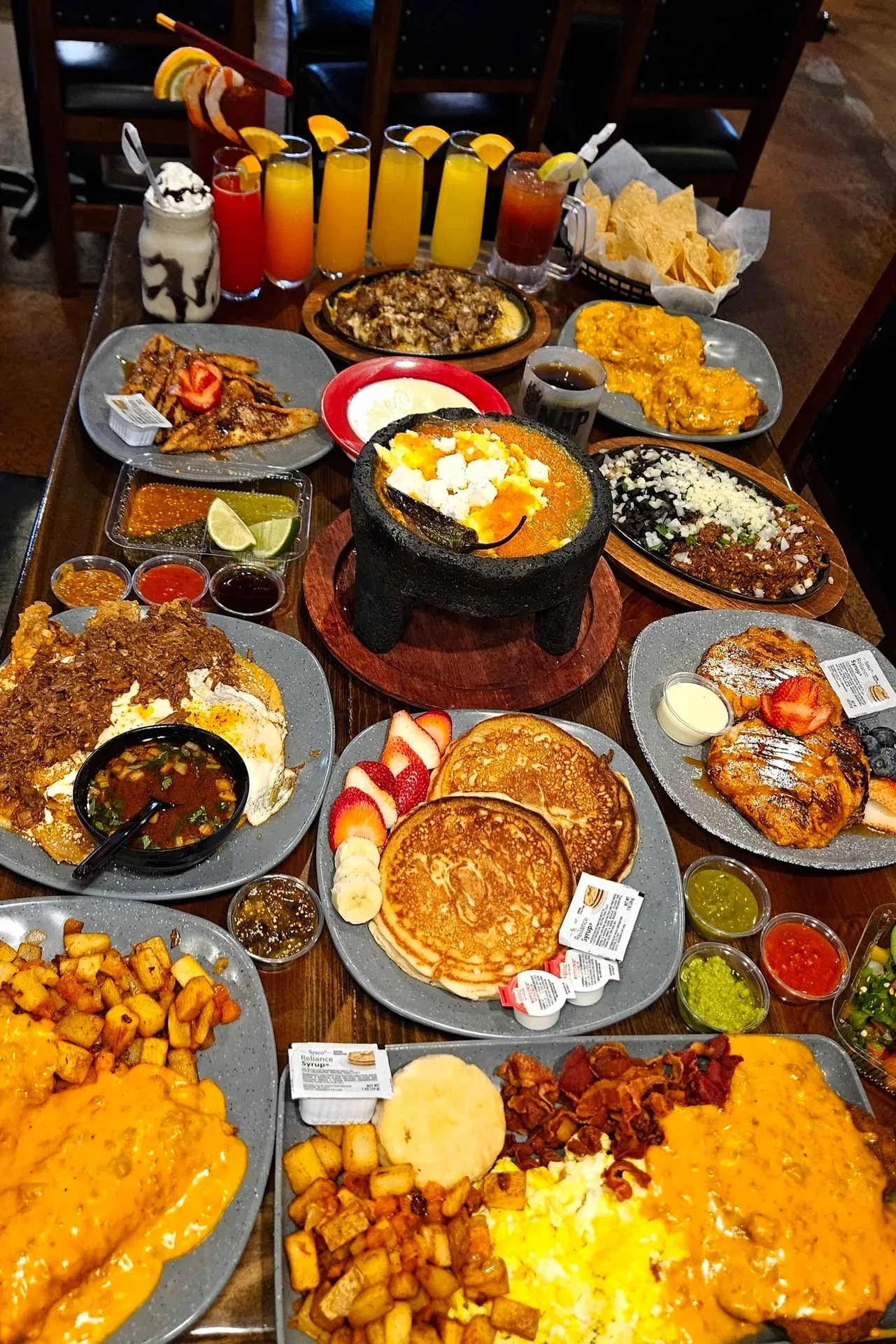 Taqueria El Rey, Augusta, GA: large Mexican breakfast/brunch spread: molcajete stone bowl dish, pancakes, home fries with queso, chilaquiles, huevos rancheros, tortilla chips, salsas, mimosas/juices lined up
