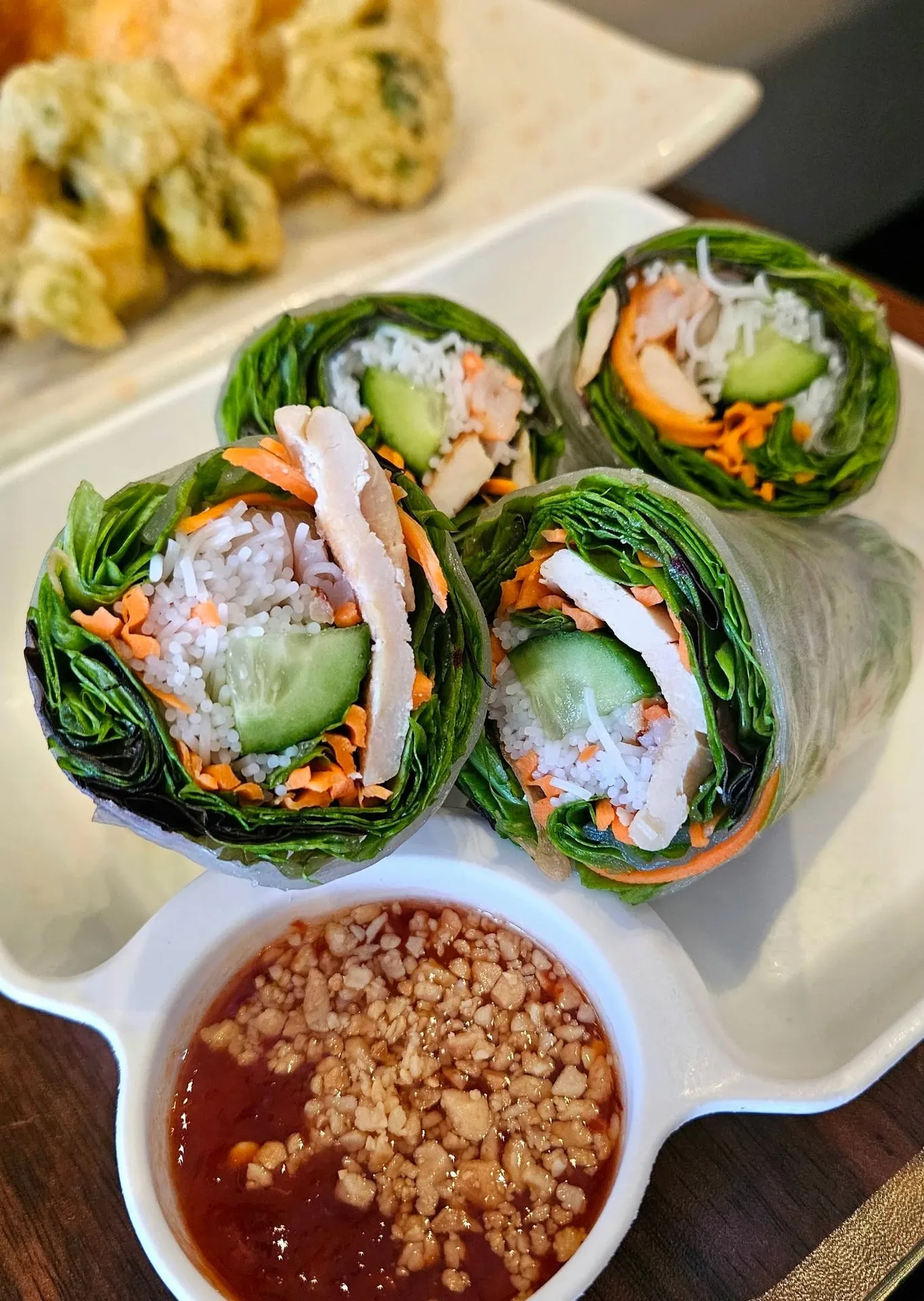 Thai Kitchen, Evans, GA: fresh Thai/Vietnamese-style spring rolls wrapped in green leaves with rice noodles, cucumber, carrot, and chicken visible in cross-section, served with a bowl of peanut dipping sauce; fried appet