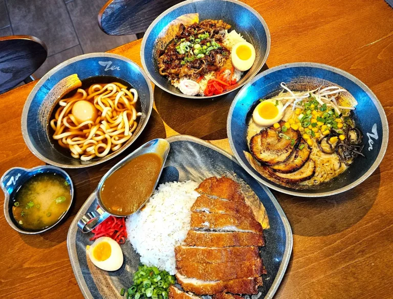 Zen Ramen And Bar, Augusta, GA: overhead view of three ramen noodle bowls with soft-boiled eggs, chashu pork, corn, bean sprouts, and udon; a bowl of miso soup; and a katsu-style breaded pork cutlet over rice with curry